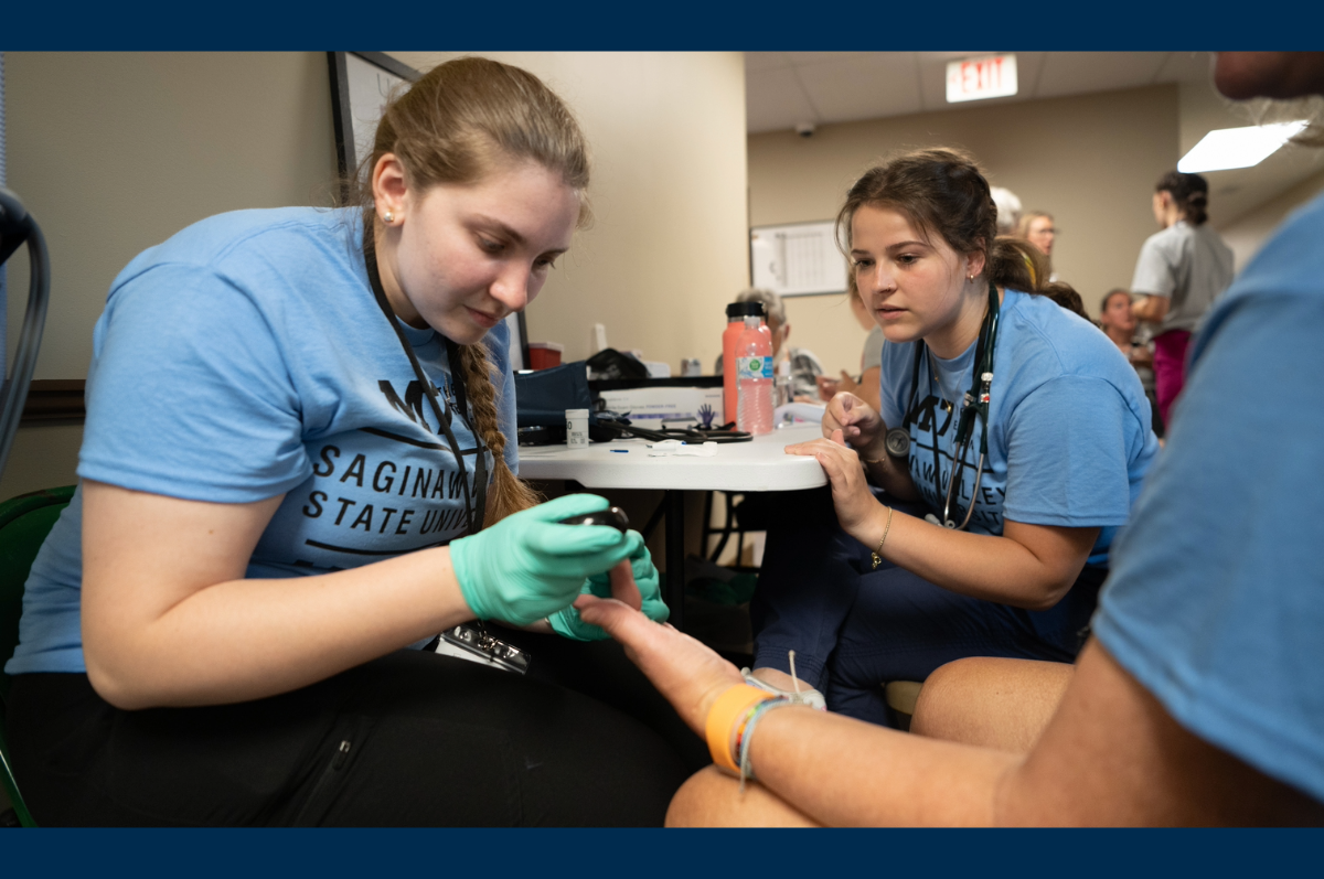 Students in blue shirts, one poking a person's finger for blood test
